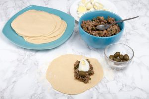 adding meat stew and egg to empanada dough circle 1