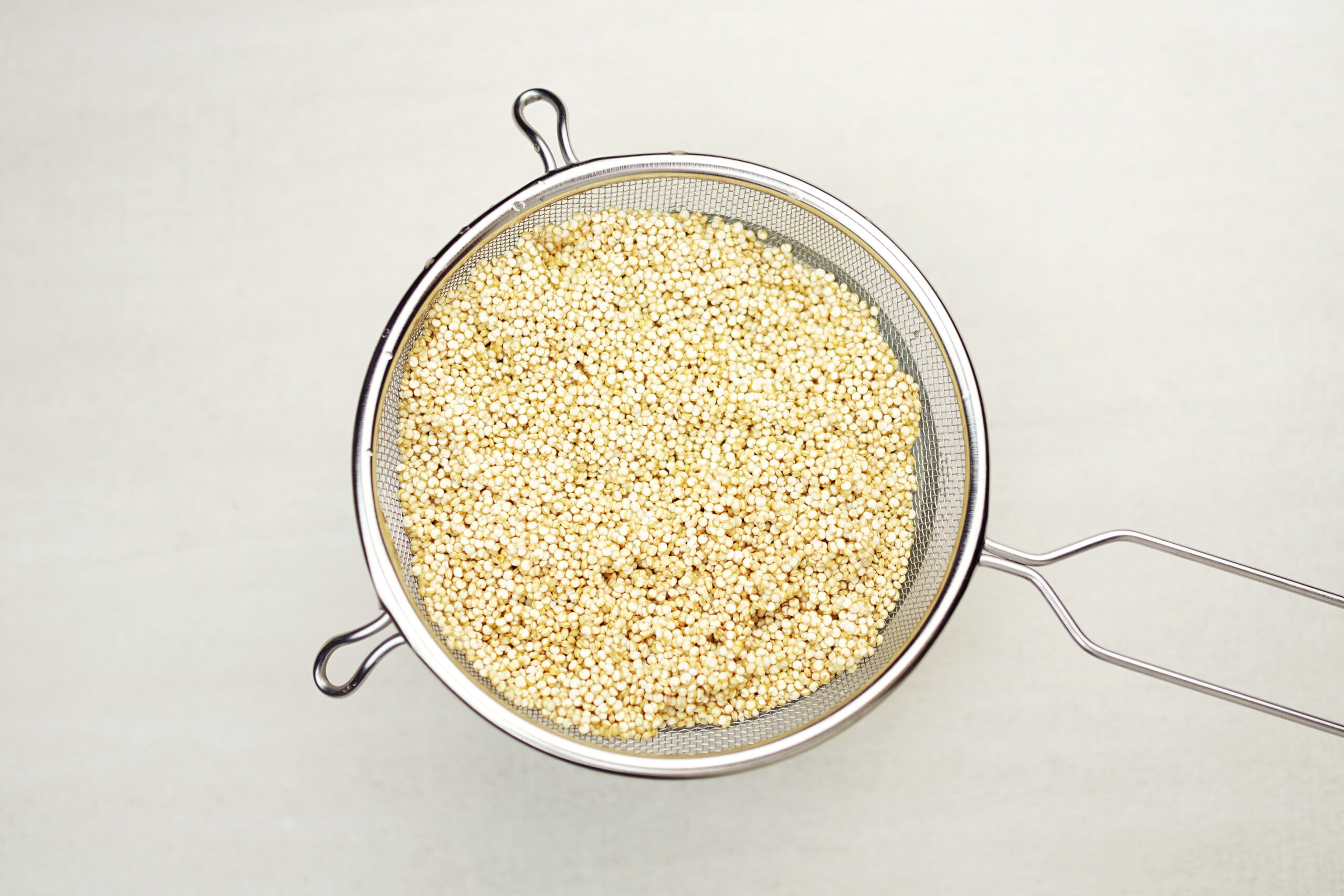Quinoa grains in mesh strainer, top view.