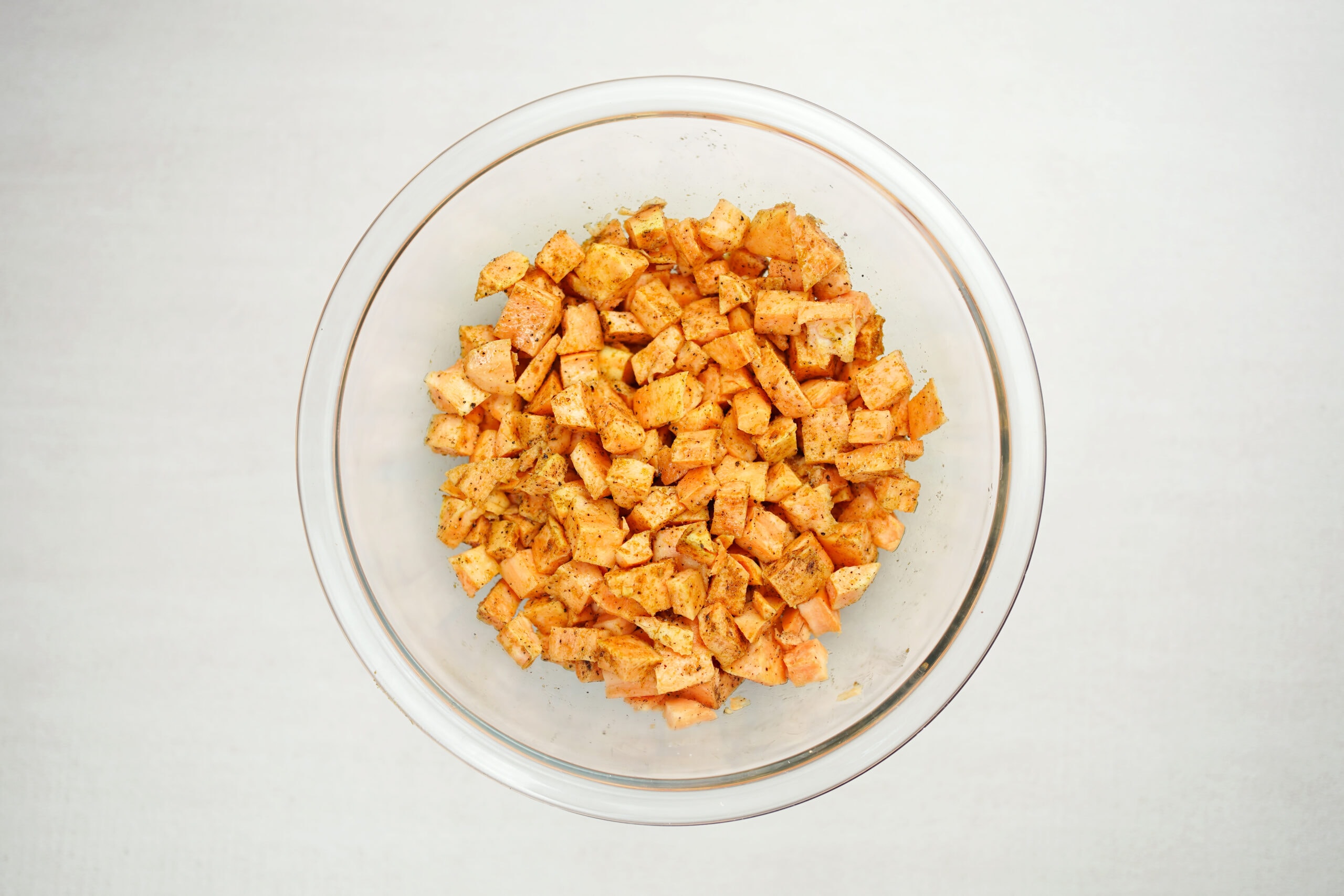 Seasoned diced sweet potatoes in glass bowl.